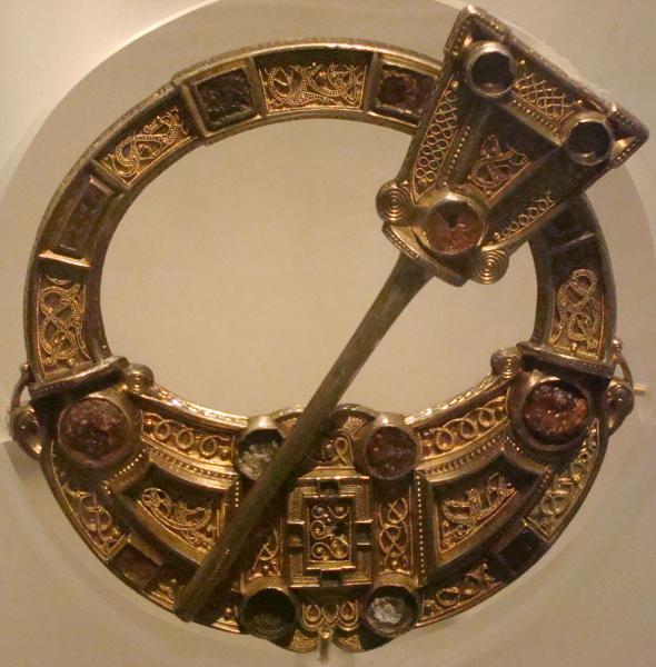 A photograph of an ornate large pennanular brooch decorated with silver and gold filigree and amber stones