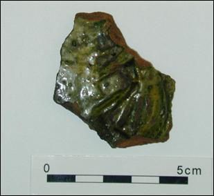 A photograph of a fragment of a decorated tile with a glossy green glaze