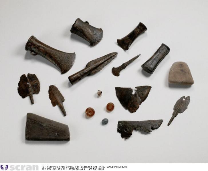 A photograph of a mixed hoard comprising metal axe heads and spearheads, fragments of sheet metal, two amber beads, one gold bead and a glass bead