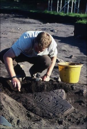 A photograph of an archaeological excavation showing a person cleaning around a slab with pictish carvings