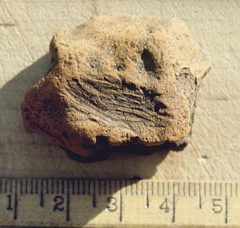 A photograph showing a lump of ochre approximately four centimetres long with scratches and chipped around some edges