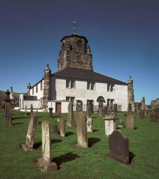 A photograph of the exterior of a whitewashed church building and graveyard with upright gravestones 