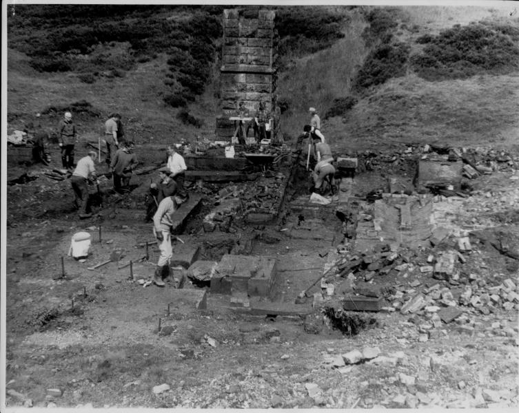 A black and white photograph showing people excavating the remains of stone built buildings