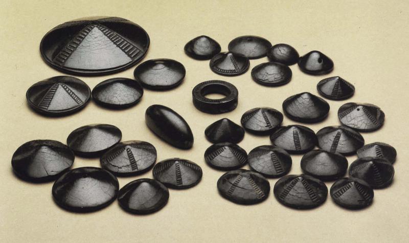 A photograph of jet artefacts comprising around 30 buttons slightly conical in shape with some decorated, a ring, and an elongated bead