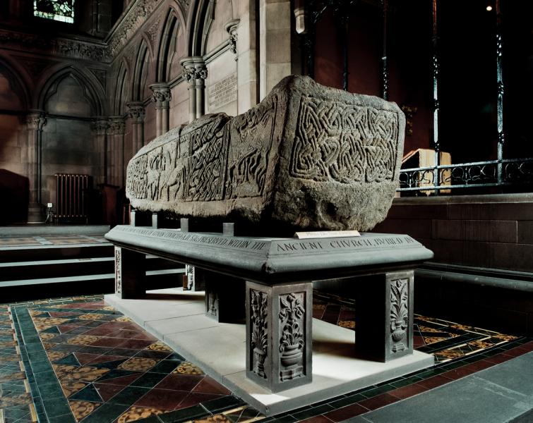 A photo of a stone sarcophagus carved with interlace and zoomorphic decoration, sat on a plinth inside a church