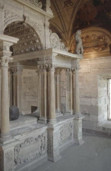 A colour photo of a stone tomb with columns, arches and scroll work, inside a church