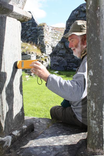 A man holding a yellow electronic tool the size and shape of a torch, against the surface of a gravestone