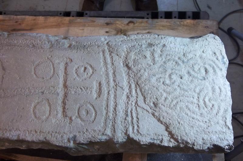 A colour photo of a stone carved with a cross, circles and Celtic interlace - with some individual chisel marks visible