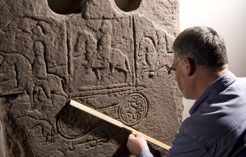 A man with a tape measure, measuring symbols and lines on a cross slab 