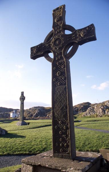 A colour photo of a large stone cross in a sunny graveyard