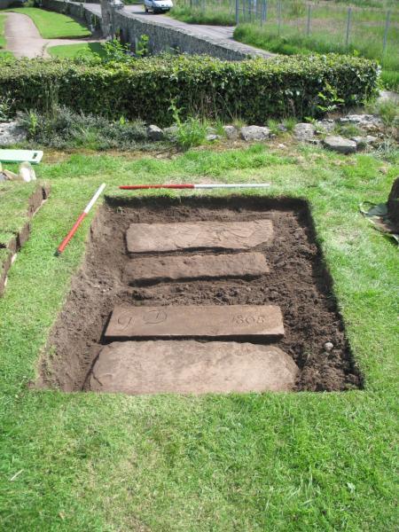 A colour photo of a small trench, with four recumbent grave slabs exposed and visible
