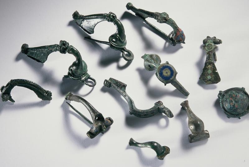 A photograph showing 11 almost complete Roman brooches of various designs, some with coloured enamel decoration