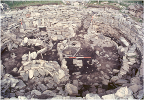 A photograph of an excavated circular dry stone structure with internal cells