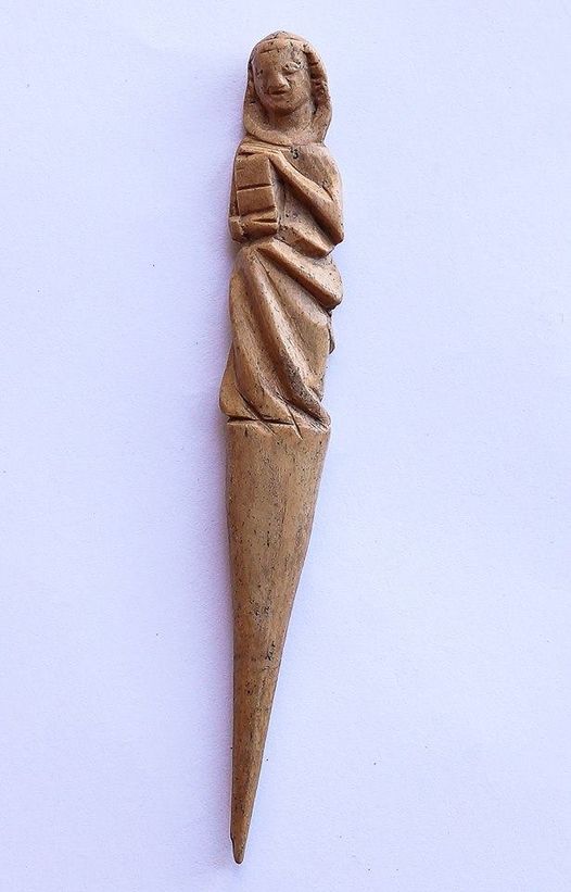 hair parter made from red deer antler. It has the shape of a tapered spike, with a carving of a person on the blunt side