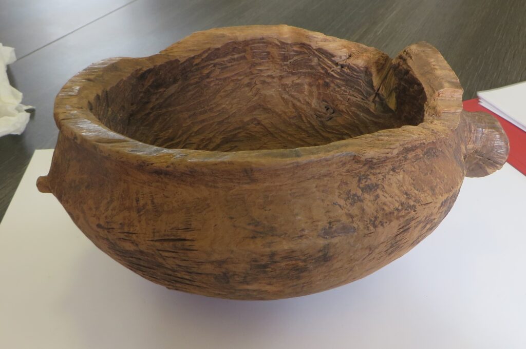 Wooden bowl bearing tool marks with a wide, flat rim, a handle on one side and a stud on the opposite side.