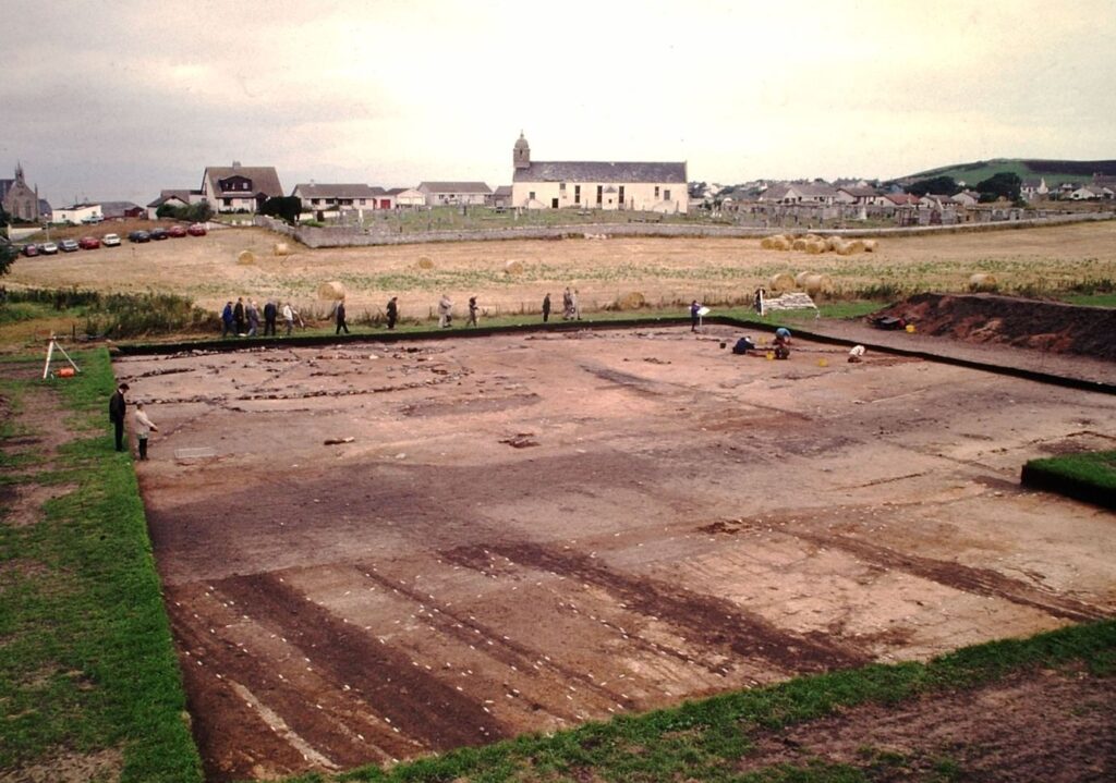 Open excavation area showing ridge and furrow marks in the foreground and stone building remains in the back.