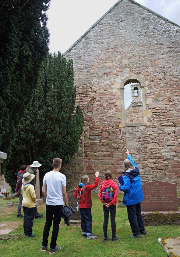Group of people standing in the graveyard and looking at the kirk.