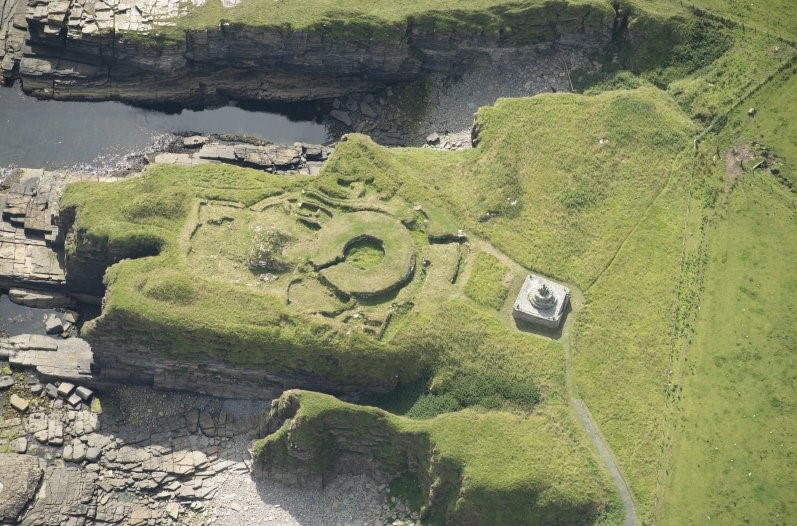 Aerial view of broch and surrounding buildings located on a promontory. 