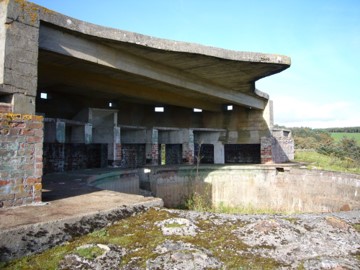 Brick and concrete structure open to the air with a large concrete-lined hole in the ground next to it.