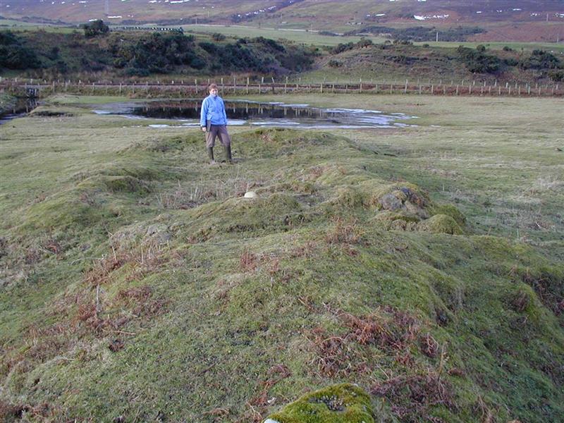 Man standing inside of the turf covered remains of the inn. 