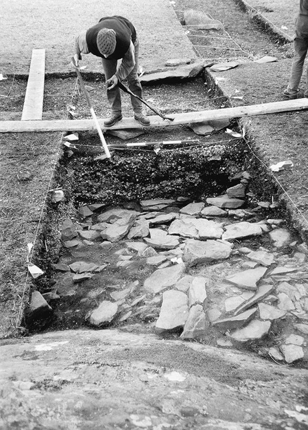 Archaeologist standing on a board over the excavation trench. 