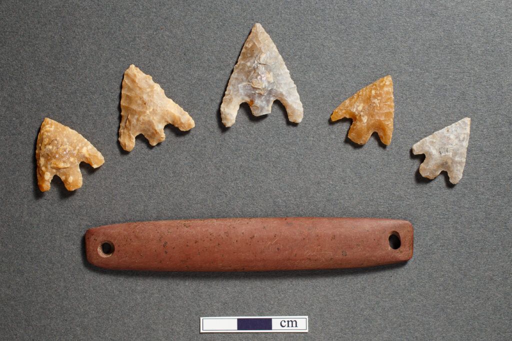 Five arrowheads placed in an arc above a stone wristguard. 