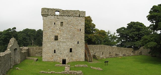Image of the front of a large castle building. It is rectangular, with small windows and a timber staircase to its right. It is surrounded by a wall. 