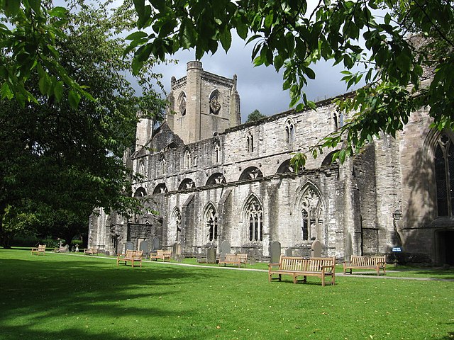 Image of a large cathedral building, build in grey stone with vaulted arcs in the walls. It is surrounded by trees and grass. 