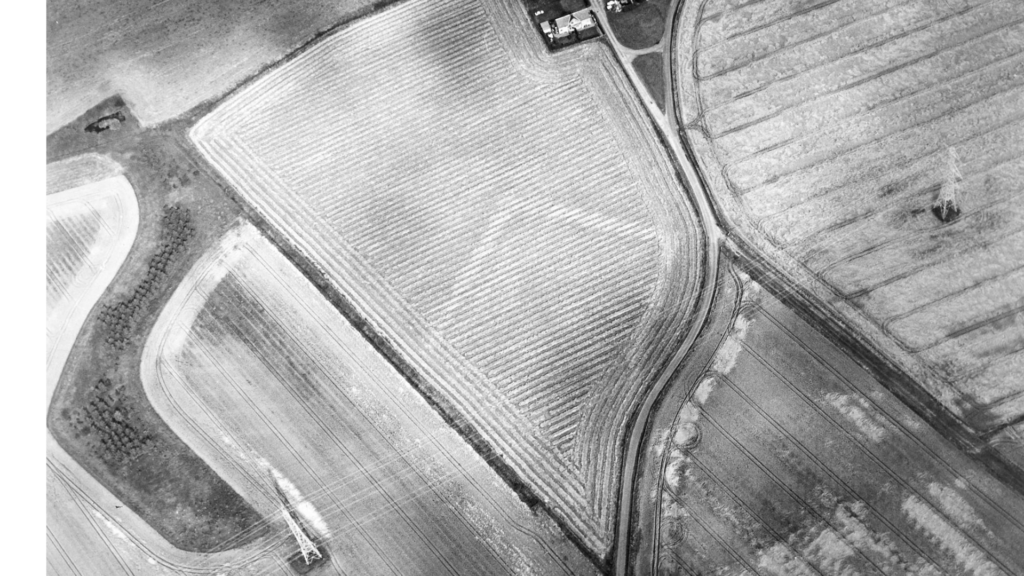 Black and white aerial image of farmland showing cropmarks in white. A large rectangular cropmark is in the centre. 
