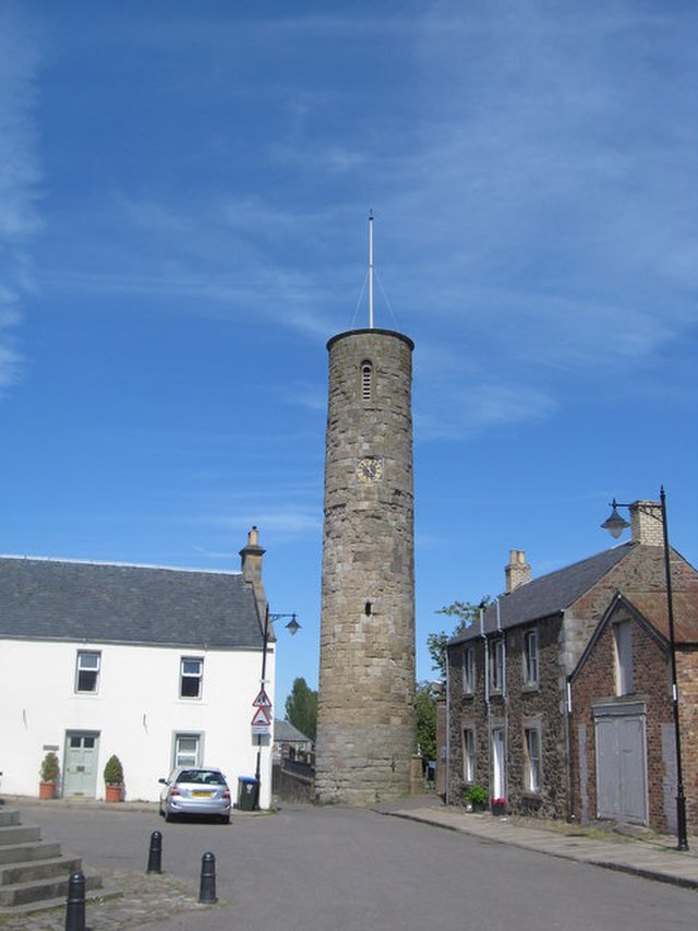 A tall, cylindrical tower with very small windows and a spike at the top. A clock is placed in the top of the tower, about one third of the way from the very top. 