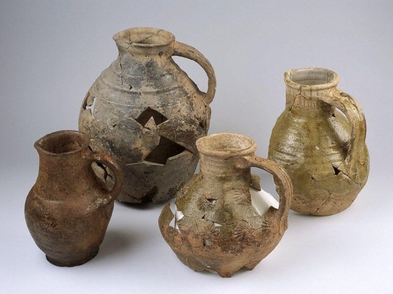Four brown pottery jugs with rounded bottoms and handles. Each one is decorated with similar lines and has a pouring spout. 