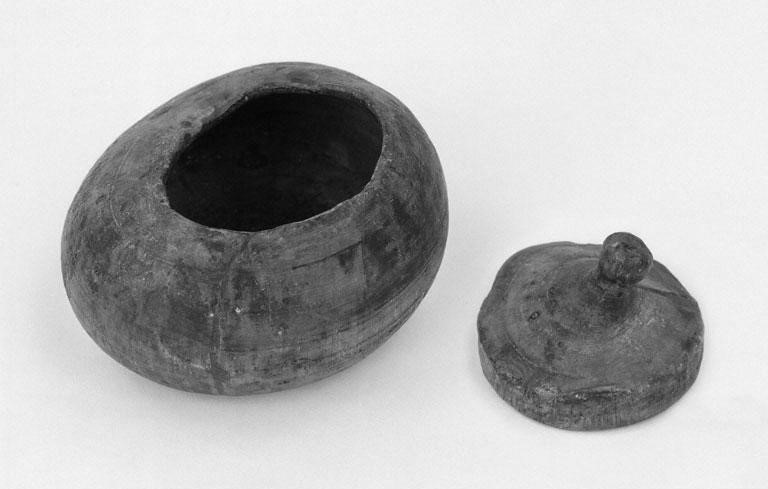 A black and white photo of a dark wood pot and lid. The pot is rounded, with a narrow round mouth at the top. The lid is round, and has a small knob at the top as a handle. 