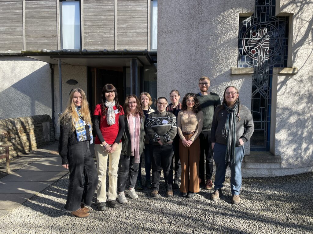 9 people stand together in front of a church hall building