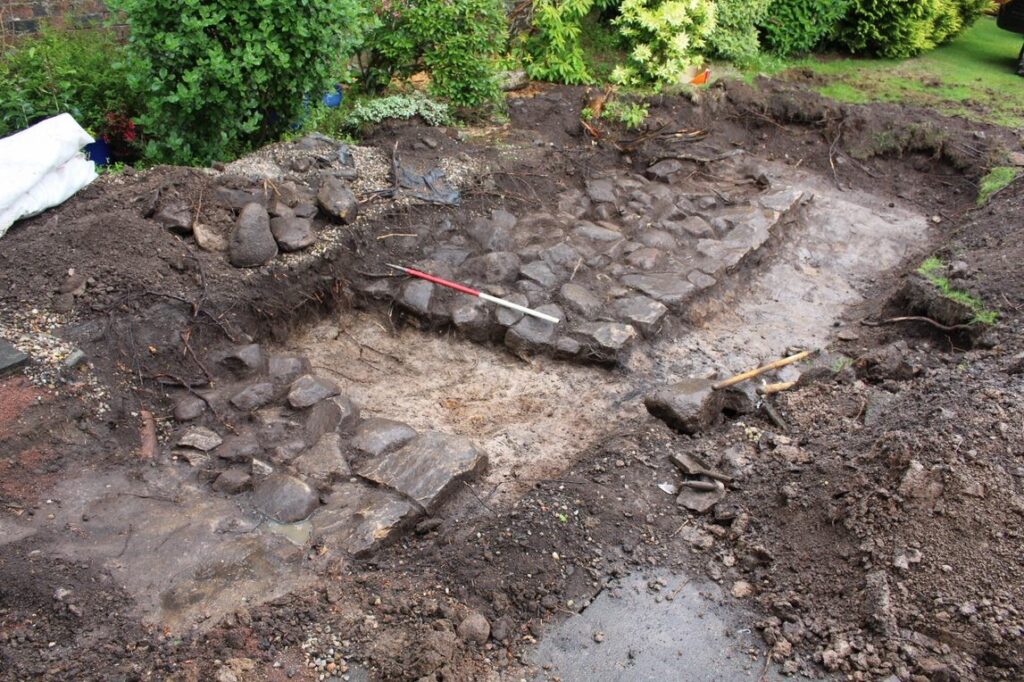 Excavation image of an open trench with a stone foundation revealed and cleaned, with metre stick for reference. 