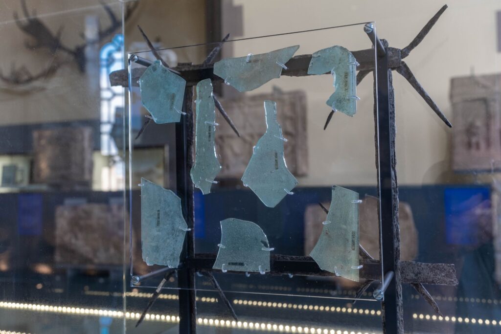 Museum image of a clear glass board with fragments of broken blue glass attached to it, showing how it would have been used. 