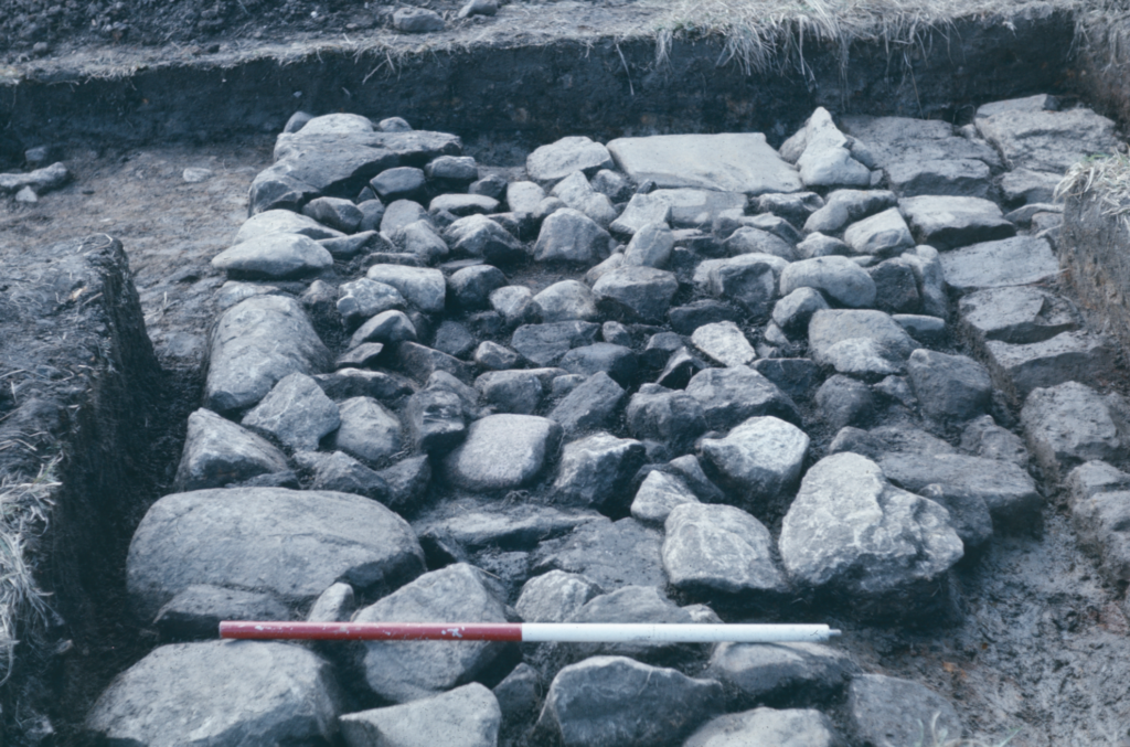 A black and white photograph of an excavation showing large stones forming a platform