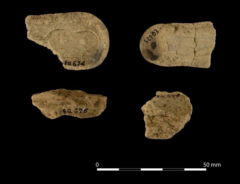 Image of four fragments of clay moulds, all yellow-brown against a black background with catalogue numbers written in black on each piece. 