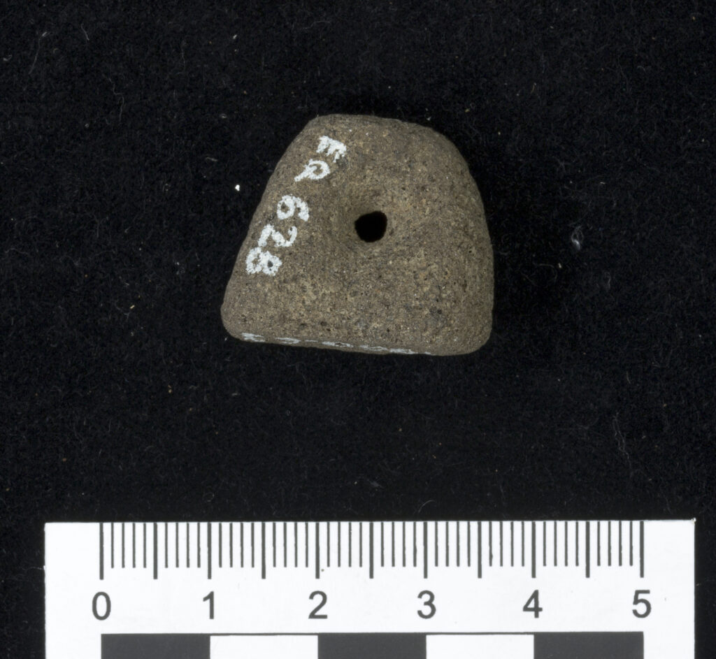 Closeup against a black background of a subrectangular stone with a hole pierced through the centre