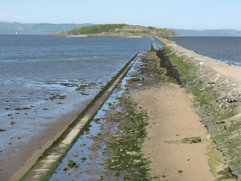 Photograph of the view of Crammond island from the mainland. In the foreground, there is a sandy beach.