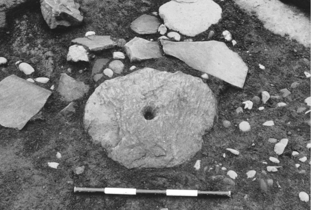 Black and white photograph of a stone rotary quern in the ground.