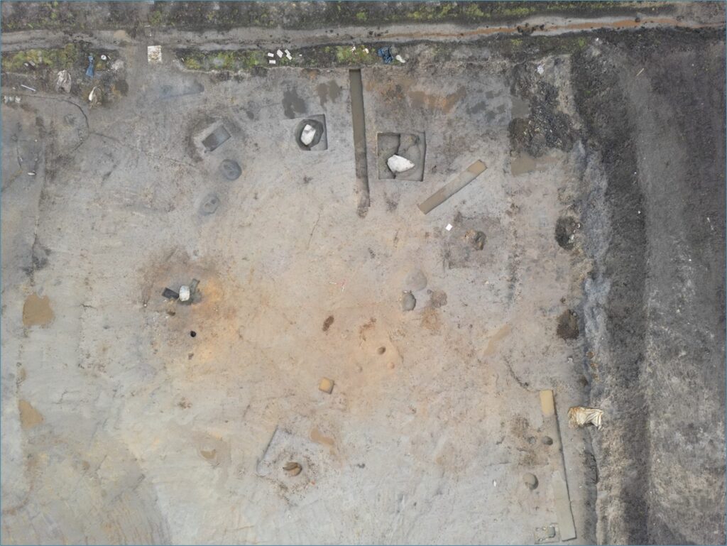 Aerial view of an open excavation trench. where some rectangular trenches have been dug deeper into the main trench, highlighting key archaeological features. 