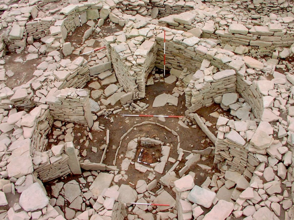 Oblique aerial view of an active excavation in a complex stone structure with a thick, round outer wall and straight internal walls which resemble the spokes of a wheel.