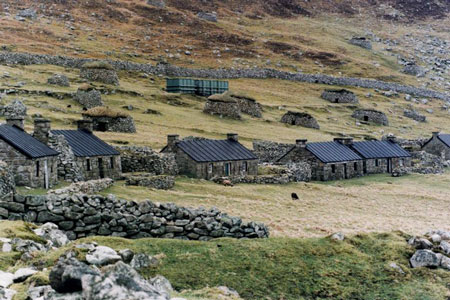 Photograph of a village of shieling style stone buidlings at the bottom of a grassy hillside.