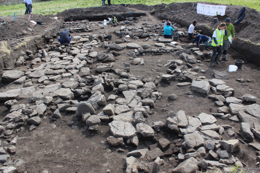 View of trench with archaeologists uncovering stones