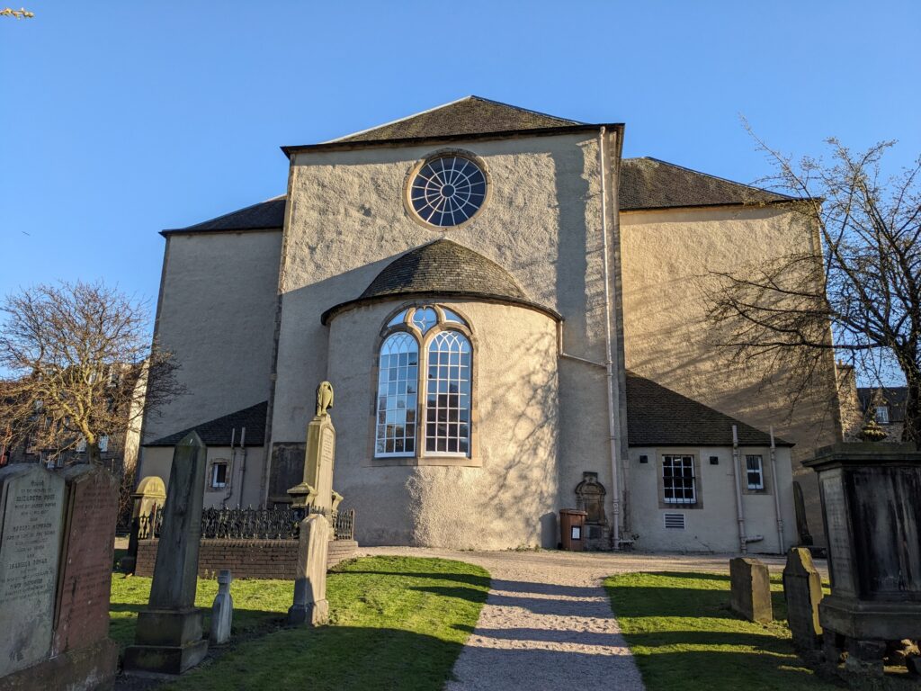Photograph of Canongate Kirk from the graveyard, with tombstones in front.