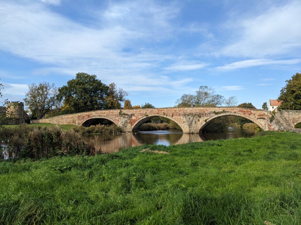 Stone bridge with 3 arches over grassy bank
