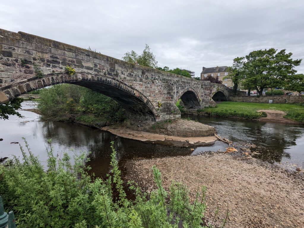 Stone bridge with arches over water and grass banks