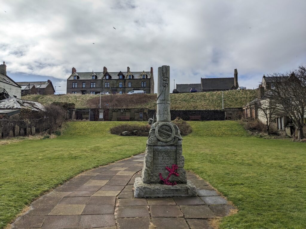 A stone memorial in the foreground with and a red poppy anchor wreath. 