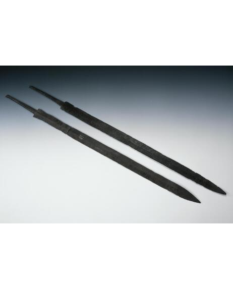 Photograph of two metal swords laid parallel against a grey / white background