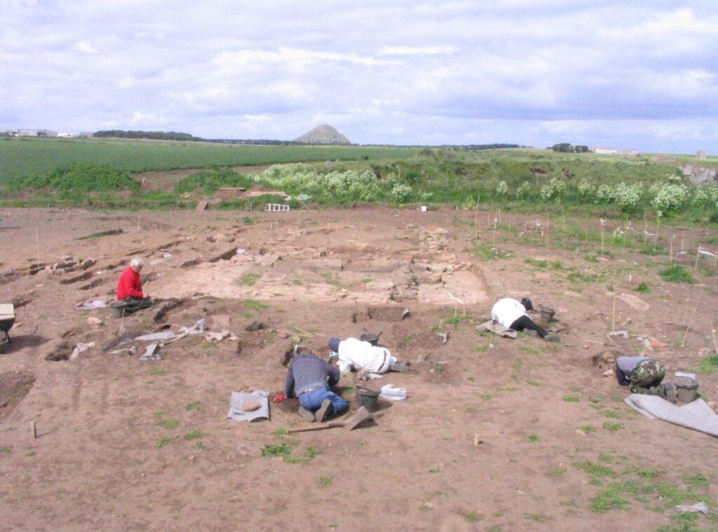 photograph of excavations with individuals excavating individual features 